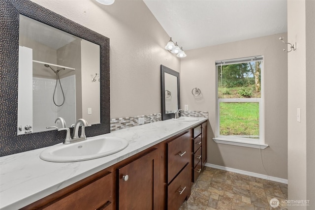 full bathroom featuring double vanity, a sink, stone finish flooring, and walk in shower