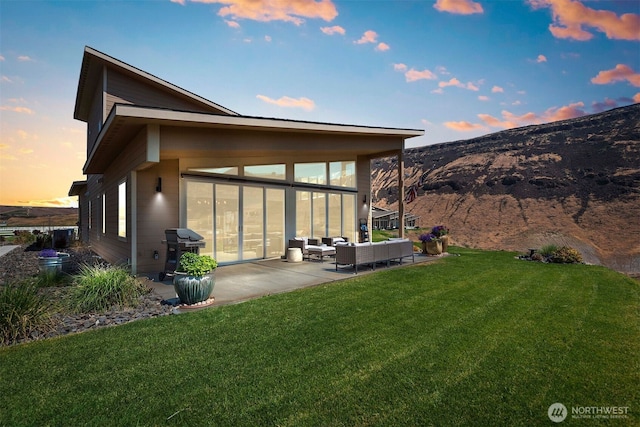 back of property at dusk with a patio area, a mountain view, a lawn, and an outdoor hangout area
