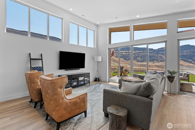 living area with light wood-style flooring, recessed lighting, baseboards, and a towering ceiling