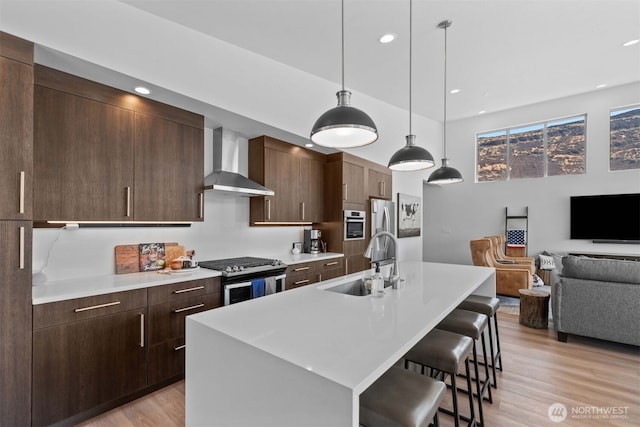 kitchen with a sink, wall chimney range hood, open floor plan, a kitchen breakfast bar, and stainless steel appliances
