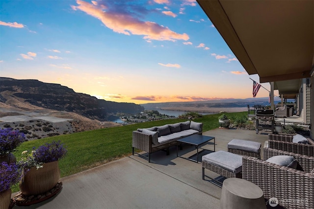 patio terrace at dusk with a yard, outdoor lounge area, and a water and mountain view