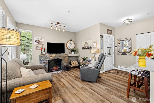 living room featuring a baseboard heating unit, baseboards, a stone fireplace, and wood finished floors