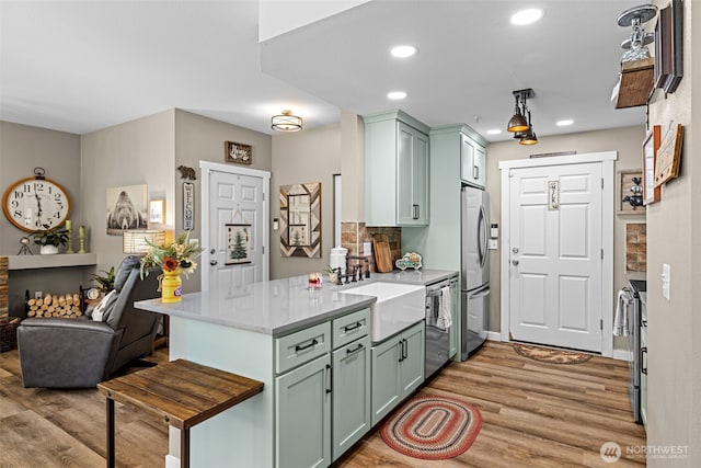kitchen featuring a peninsula, green cabinetry, stainless steel fridge, and light wood-type flooring