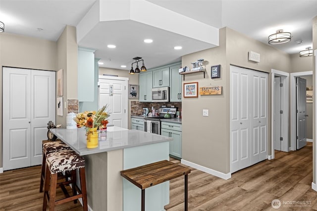 kitchen with light wood finished floors, stainless steel appliances, a peninsula, and a breakfast bar area