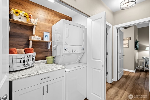 washroom featuring stacked washer and dryer, baseboards, laundry area, and dark wood finished floors
