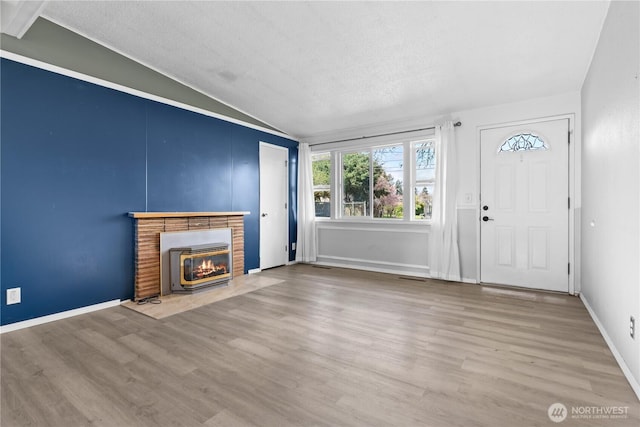 unfurnished living room featuring baseboards, a fireplace, wood finished floors, and lofted ceiling