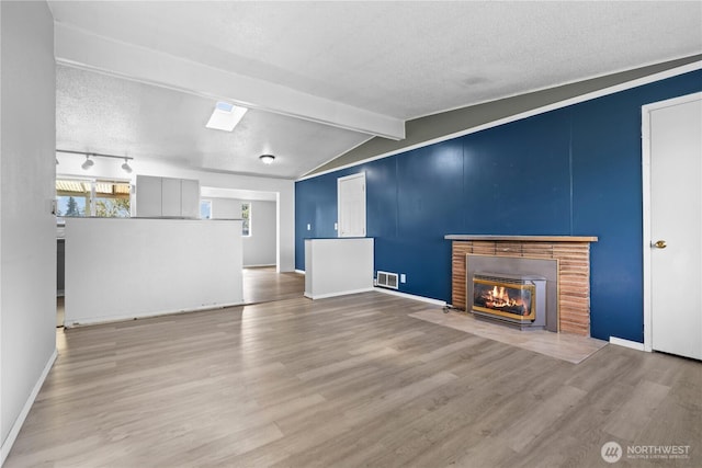 unfurnished living room featuring vaulted ceiling with beams, wood finished floors, a brick fireplace, a textured ceiling, and baseboards