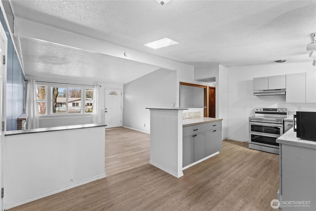 kitchen with a textured ceiling, light wood-style flooring, vaulted ceiling with skylight, under cabinet range hood, and double oven range