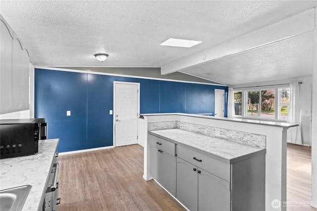 kitchen with a sink, black microwave, lofted ceiling with beams, a textured ceiling, and light wood-style flooring