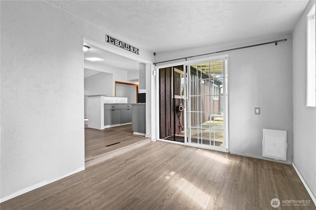 unfurnished room featuring a textured ceiling, visible vents, baseboards, wood finished floors, and a textured wall