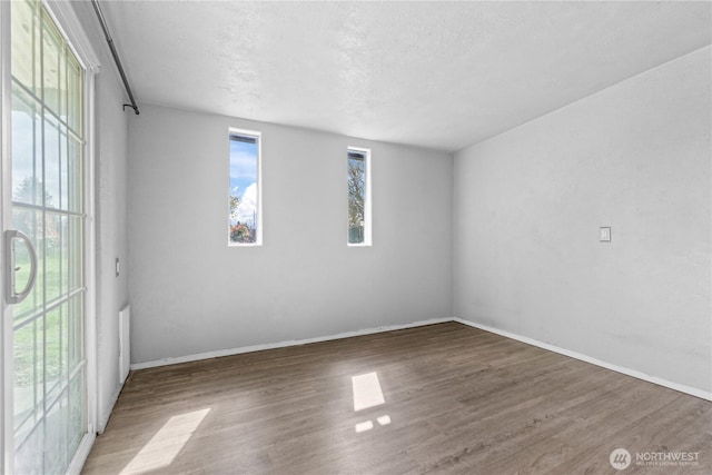 empty room with a textured ceiling, baseboards, and wood finished floors