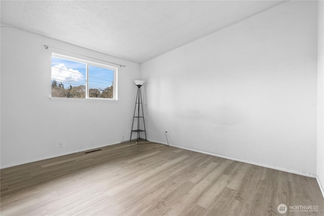 spare room with wood finished floors, a textured ceiling, and visible vents
