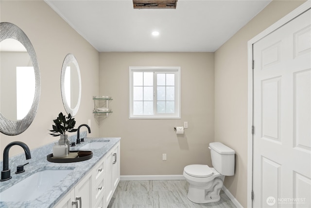 bathroom with baseboards, toilet, double vanity, and a sink