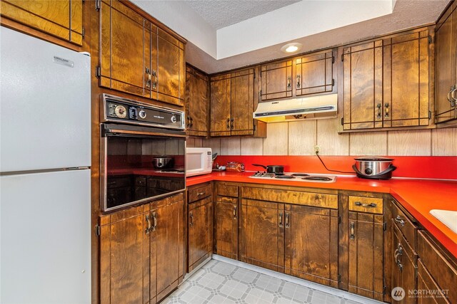 192 Meade Hill Rd, Glenoma, WA 98336 - kitchen with white appliances, under cabinet range hood, light floors, and a textured ceiling