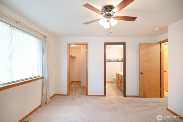 unfurnished bedroom with a closet, a spacious closet, light colored carpet, and baseboards