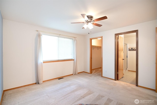 unfurnished bedroom with a walk in closet, light carpet, baseboards, and visible vents