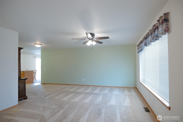 empty room featuring visible vents, baseboards, a ceiling fan, and light carpet