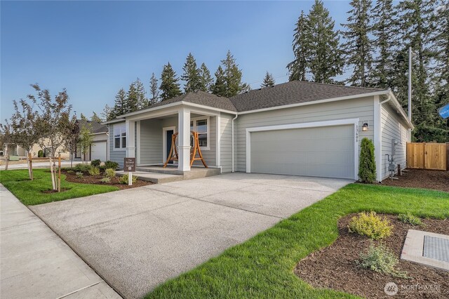 view of front of home featuring covered porch, concrete driveway, fence, an attached garage, and a shingled roof