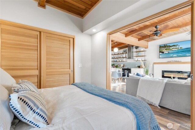 bedroom featuring wood ceiling, wood finished floors, beamed ceiling, a closet, and a glass covered fireplace