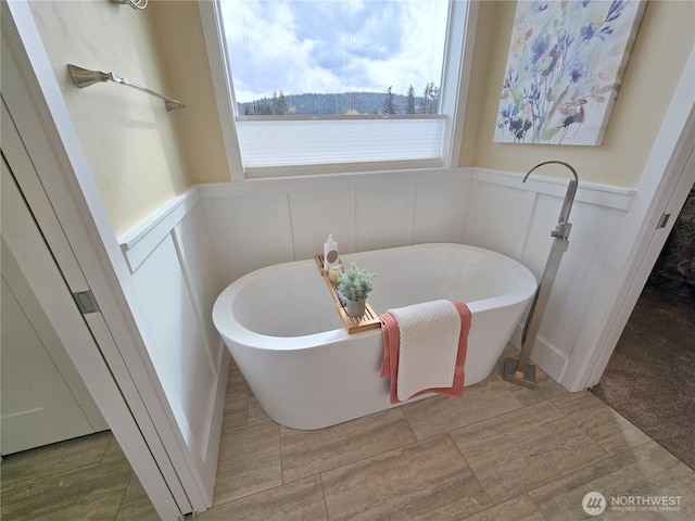 full bathroom featuring a wainscoted wall, a freestanding bath, and a decorative wall