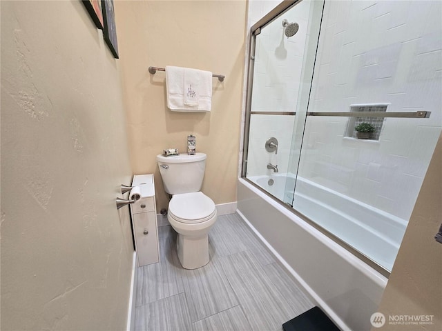 bathroom with toilet, shower / bath combination with glass door, and baseboards