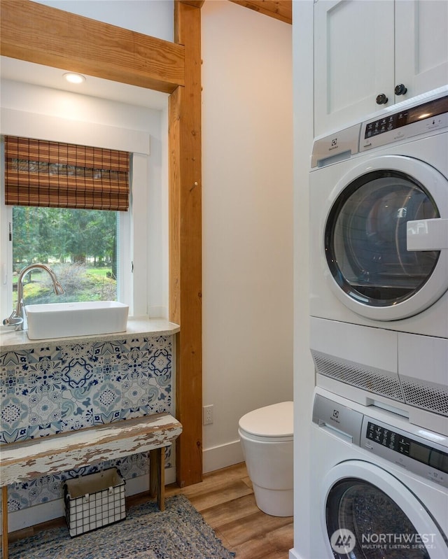 washroom featuring stacked washer / drying machine, a sink, light wood-type flooring, laundry area, and baseboards