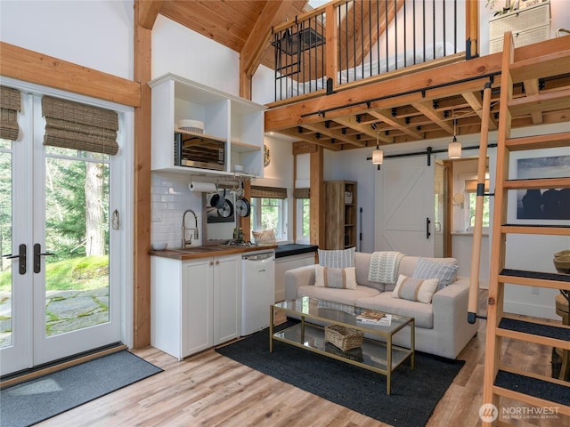 living area with plenty of natural light, high vaulted ceiling, a barn door, and light wood finished floors