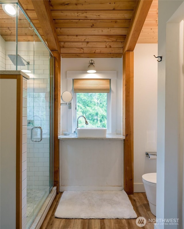 bathroom with beamed ceiling, wood finished floors, toilet, a stall shower, and wooden ceiling