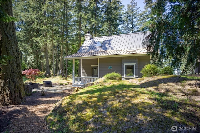 rear view of property featuring a chimney, a porch, a standing seam roof, and metal roof
