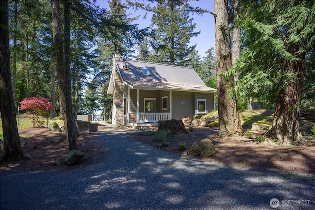 view of front of home with stone siding, metal roof, a porch, and driveway