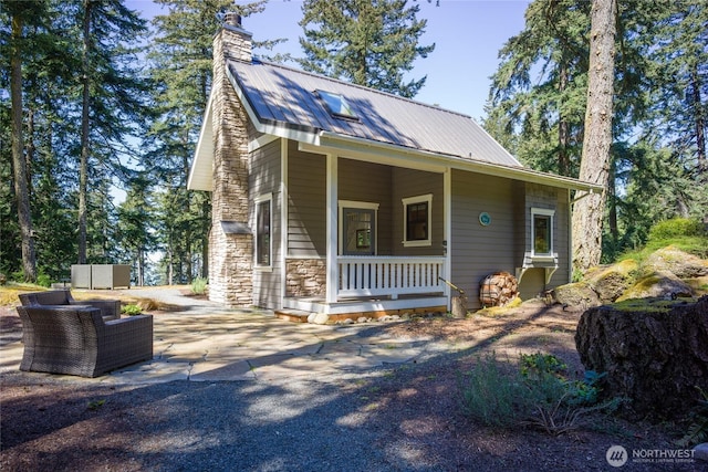view of front of house with stone siding, a chimney, metal roof, and a porch