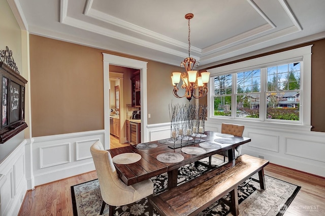 dining space featuring a raised ceiling, a decorative wall, crown molding, wainscoting, and a notable chandelier