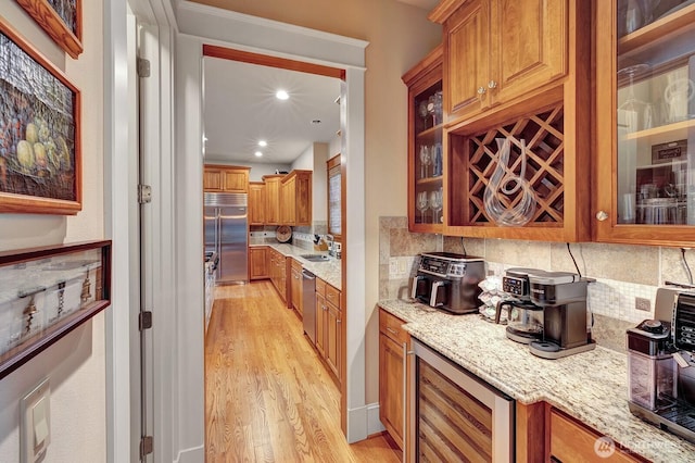 bar with beverage cooler, light wood finished floors, stainless steel appliances, a sink, and decorative backsplash