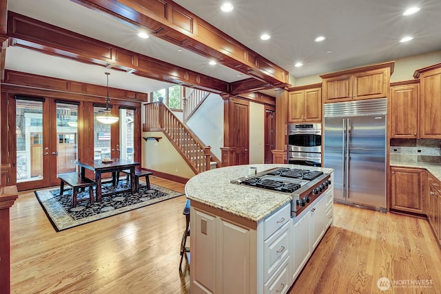 kitchen with stainless steel appliances, a center island, french doors, light wood-style flooring, and light stone countertops