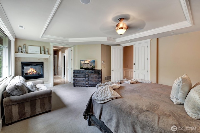 carpeted bedroom with visible vents, a glass covered fireplace, and a tray ceiling