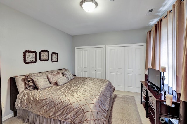 bedroom featuring two closets, visible vents, and light colored carpet
