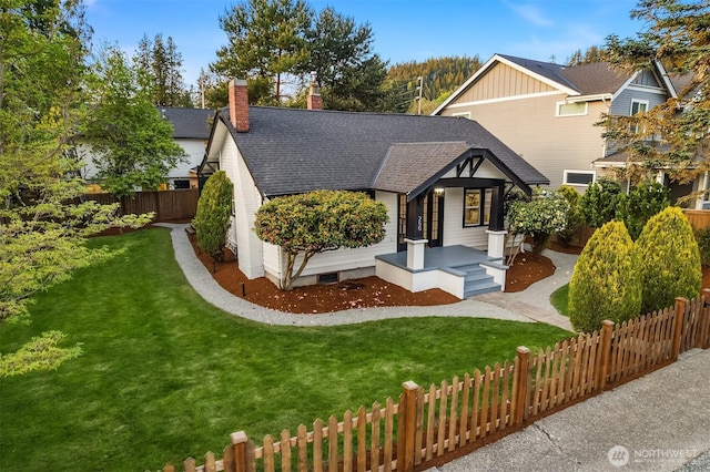 tudor-style house featuring a shingled roof, a chimney, fence private yard, and a front yard