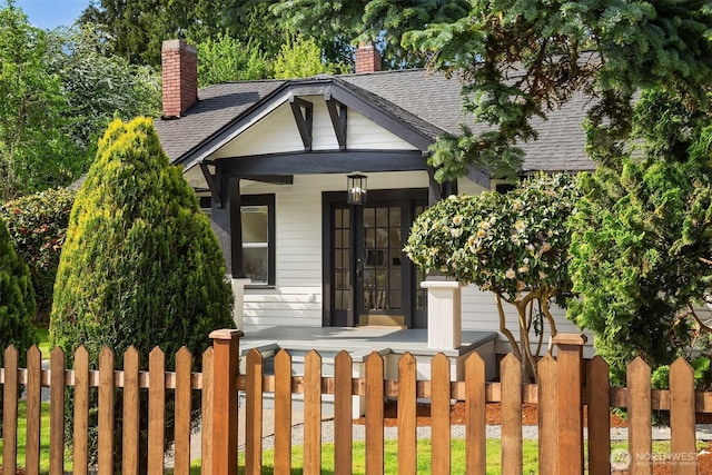bungalow-style home featuring roof with shingles, covered porch, a fenced front yard, and a chimney