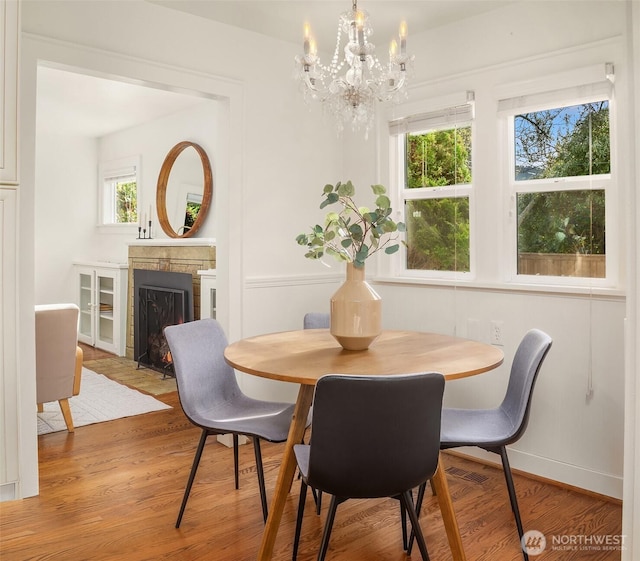 dining space with a fireplace with flush hearth, wood finished floors, and a notable chandelier