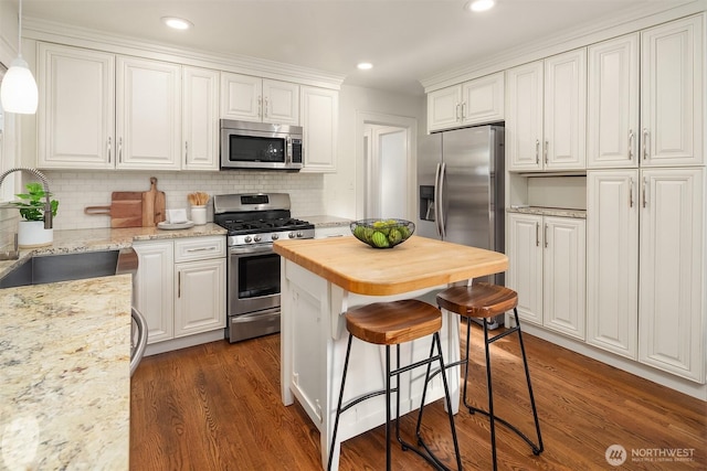 kitchen featuring a kitchen bar, appliances with stainless steel finishes, a sink, white cabinets, and wood counters
