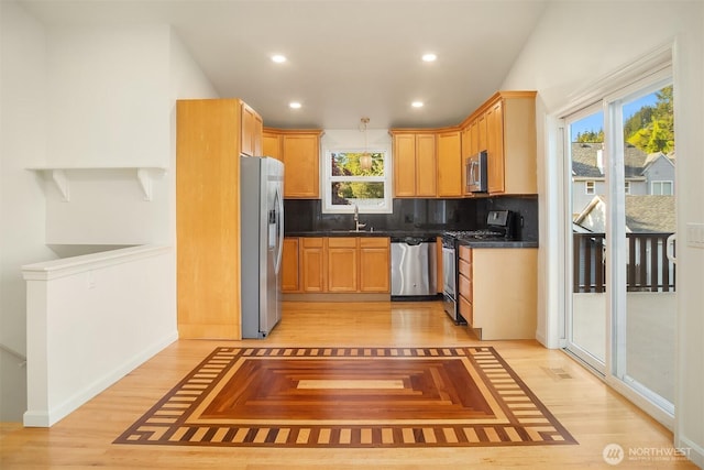 kitchen featuring dark countertops, a sink, light wood finished floors, stainless steel appliances, and tasteful backsplash