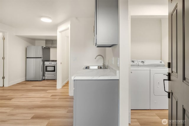 washroom featuring laundry area, a sink, baseboards, light wood-type flooring, and washer and clothes dryer