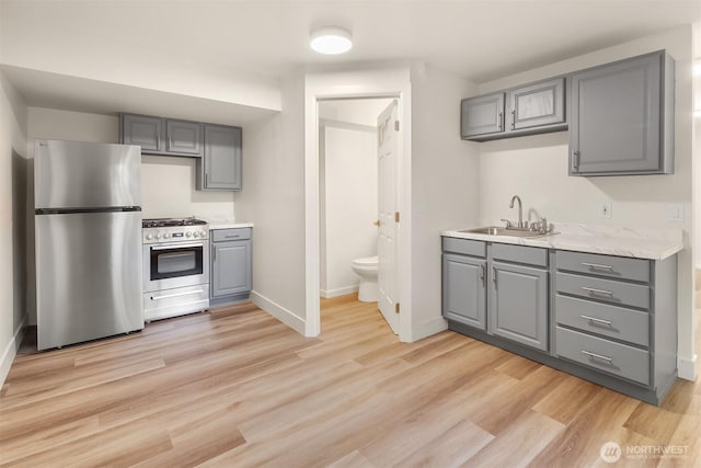 kitchen featuring gray cabinets, a sink, light countertops, stainless steel appliances, and light wood-style flooring