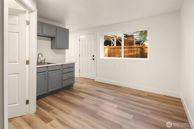 kitchen with light wood-style floors, baseboards, light countertops, gray cabinets, and a sink