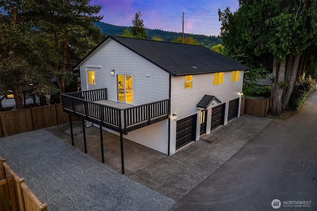 back of property featuring a garage, fence, a wooden deck, and a shingled roof