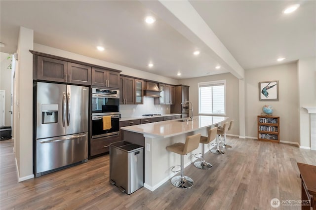 26334 203rd Pl SE, Covington, WA 98042 - kitchen with appliances with stainless steel finishes, dark brown cabinets, premium range hood, a kitchen island with sink, and a breakfast bar area