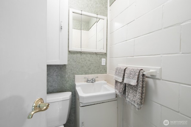 bathroom featuring toilet, vanity, and wallpapered walls