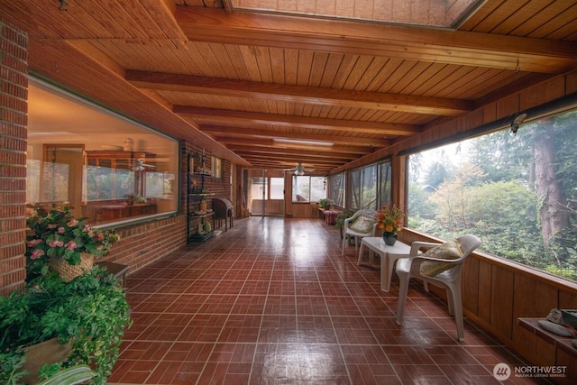 unfurnished sunroom with brick floor, a ceiling fan, wooden ceiling, and beam ceiling