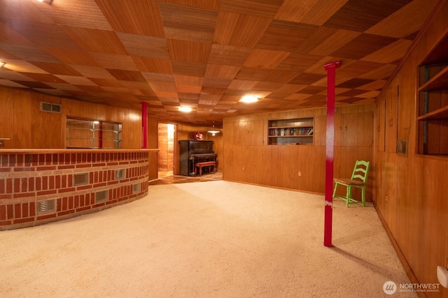 finished below grade area featuring visible vents, a bar, a wood stove, carpet, and wooden walls