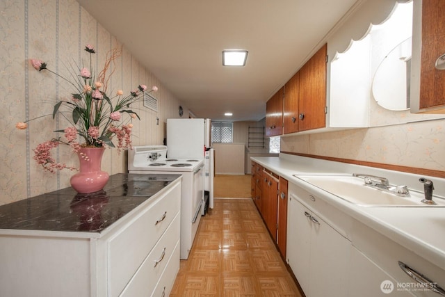 kitchen featuring brown cabinetry, white appliances, a sink, and wallpapered walls